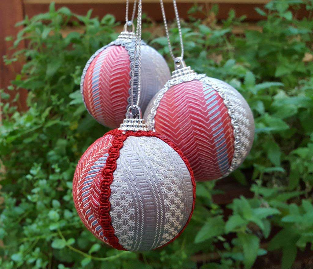 Tre palline decorative appese a dei fili argentati, realizzate con palline di polistirolo, tessuto di cravatte e nastrini.