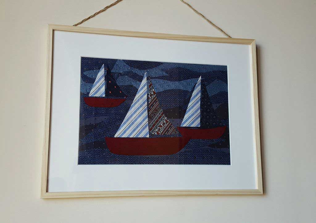 Un quadro in cornice di legno di tre barche a vela in mezzo al mare.