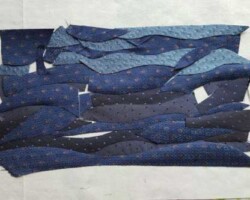 Le onde del mare ritagliate sono disposte su una base di stoffa per essere incollate, al fine di creare lo sfondo.